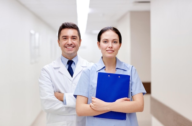 clínica, profesión, personas, atención médica y concepto de medicina - médicos sonrientes o médicos con portapapeles en el pasillo del hospital