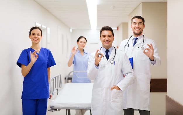 clínica, profesión, personas, atención de la salud y concepto de medicina - grupo de médicos felices o médicos con camilla mostrando el signo de la mano en el pasillo del hospital