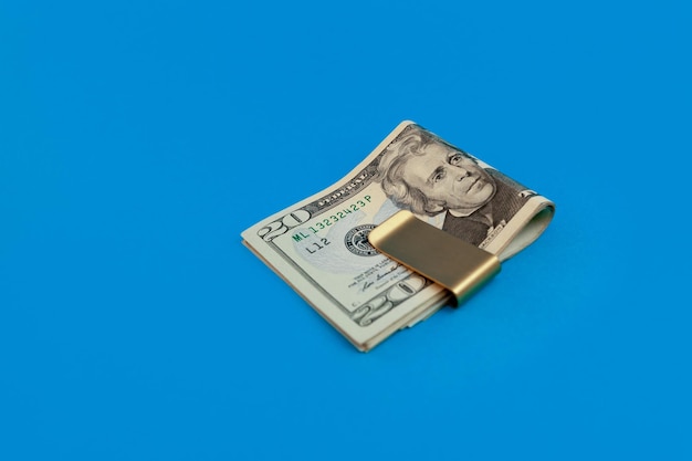 Clip de dinero con billetes de dólar sobre fondo azul.