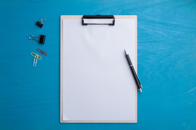 clipboad con papel en blanco y lápiz en la mesa de madera azul