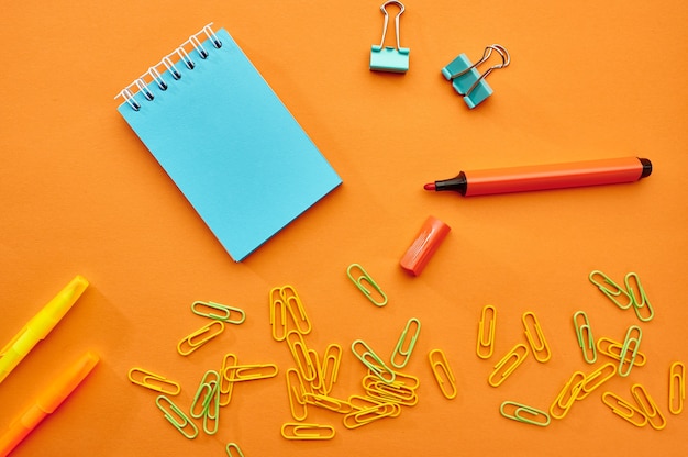 Clipes de papel, bloco de notas e close up do marcador em fundo laranja. Material de papelaria para escritório, acessórios escolares ou educacionais, ferramentas de escrita e desenho