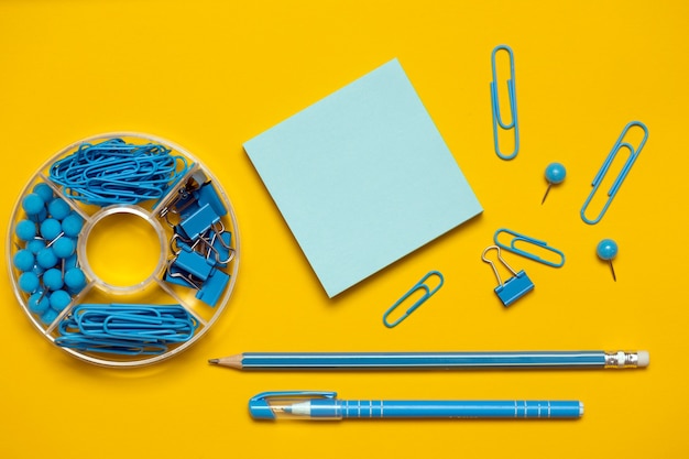 Clipes de papel de papelaria, fichários, botões, lápis, caneta e papel em azul sobre fundo amarelo