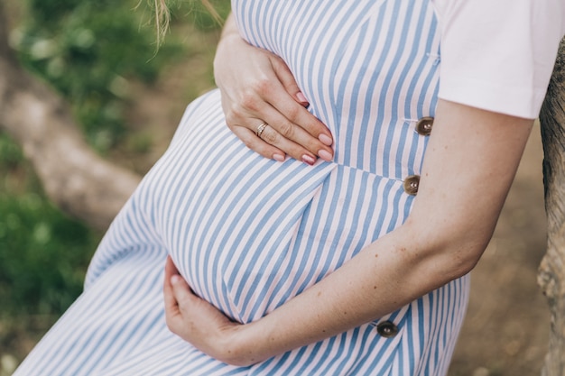 Close da barriga de uma menina grávida, uma jovem mãe acaricia sua barriga com as mãos grávidas ...