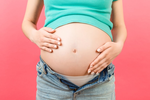 Close da barriga de uma mulher grávida nua usando jeans abertos