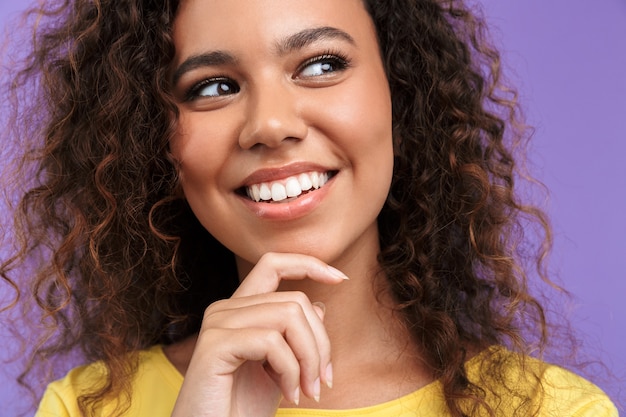 Close da imagem de uma linda mulher afro-americana com cabelo encaracolado sorrindo isolada sobre a parede violeta