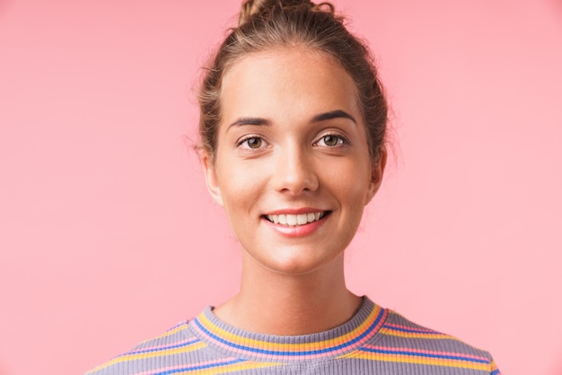 Close da imagem positiva de uma linda mulher vestida com roupas coloridas e sorrindo com um olhar feliz isolada sobre a parede rosa