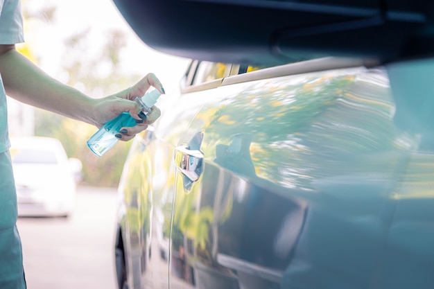 Close da mão da mulher está pulverizando álcool, spray desinfetante na maçaneta da porta do carro. contaminação de germes covid-19 vírus e conceito de higiene pessoal.