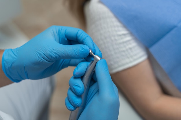 Close da mão de um dentista com luvas azuis segurando uma ferramenta