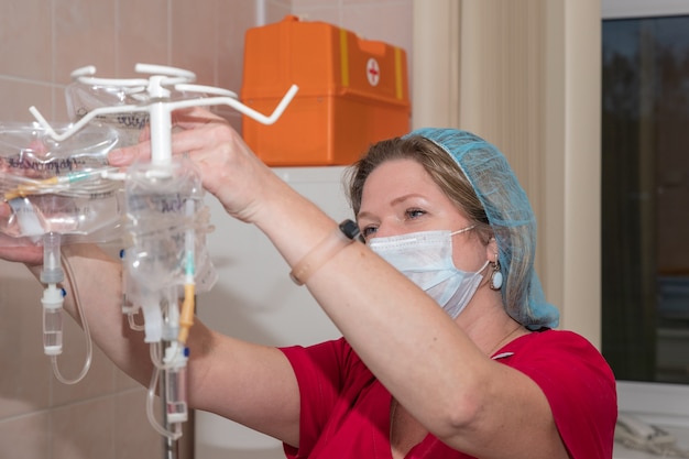 Close da mão de uma enfermeira ajustando o conta-gotas de soro fisiológico em um hospital. médica do hospital com gotejamento iv. gotejamento para estimular a paciente