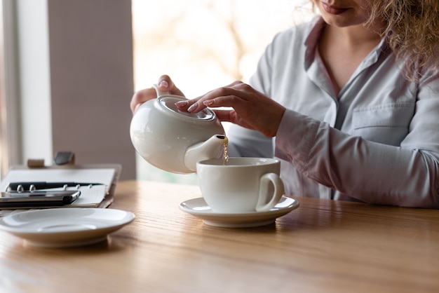 Close da mão de uma garota que se serve de chá. café da manhã no café.