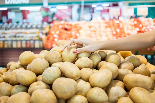 Close da mão de uma jovem pegando batata no supermercado