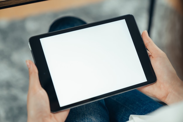 Close da mão de uma mulher segurando o tablet digital na mesa e a tela está em branco.