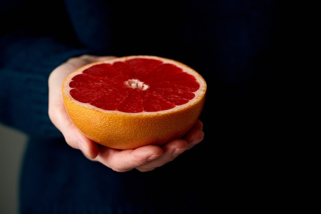 Close da mão de uma mulher segurando uma toranja fresca de frutas cítricas vermelhas cortadas ao meio