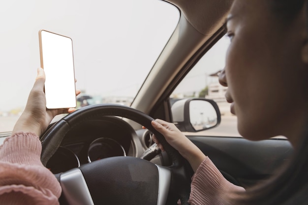 Foto close da mão segurando o smartphone com maquete branca no fundo da tela do volante do carro