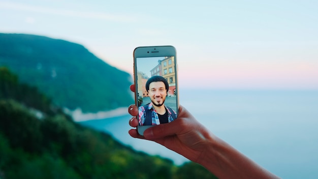 Close da mão segurando o smartphone durante a videochamada com o homem em frente ao mar.