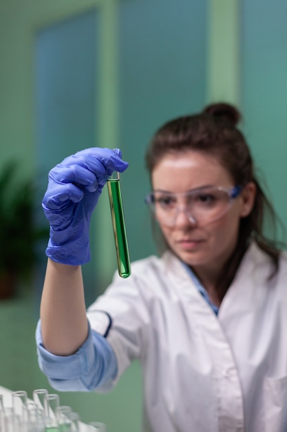 Close da mulher cientista olhando para o tubo de ensaio com amostra de dna examinando para experimento de microbiologia. Biólogo pesquisador trabalhando em um laboratório agrícola, desenvolvendo experiência em gmo em plantas.