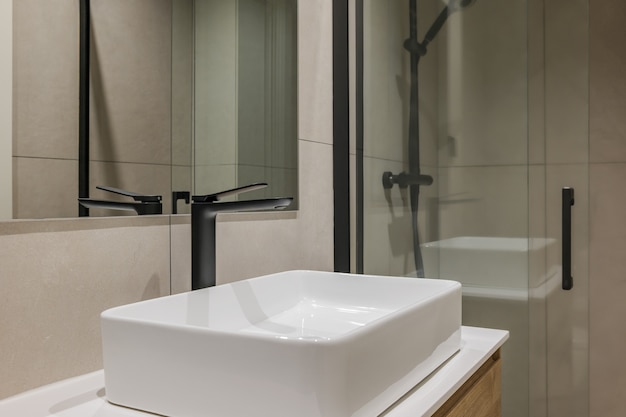 Close da pia branca com torneira preta e espelho no interior do banheiro de estilo moderno em reformado.