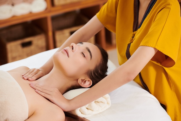 Close da terapeuta fazendo massagem para uma jovem enquanto ela está deitada na cama com os olhos fechados