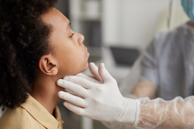 Close da vista lateral de um médico irreconhecível examinando um garoto afro-americano em busca de cobiça durante uma consulta na clínica