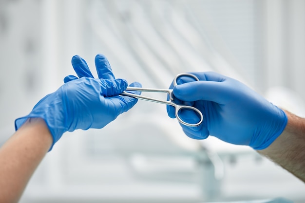 Close das mãos de um dentista e enfermeiro cirurgião sobre uma sala de cirurgia durante uma operação de implante dentário