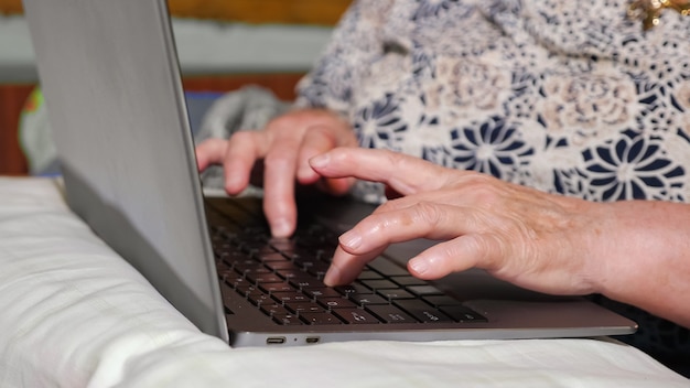 Close das mãos de uma mulher idosa digitando em um laptop