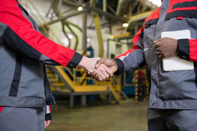 Close de capatazes multiétnicos irreconhecíveis em um aperto de mão uniforme em uma fábrica