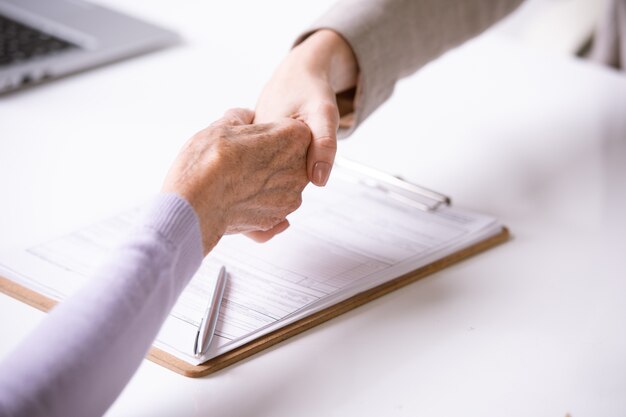 Foto close de consultor fazendo aperto de mão com mulher aposentada após assinar documento