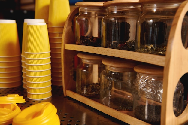 Close de copos de papelão amarelos invertidos em uma máquina de café e recipientes de copos transparentes com chá