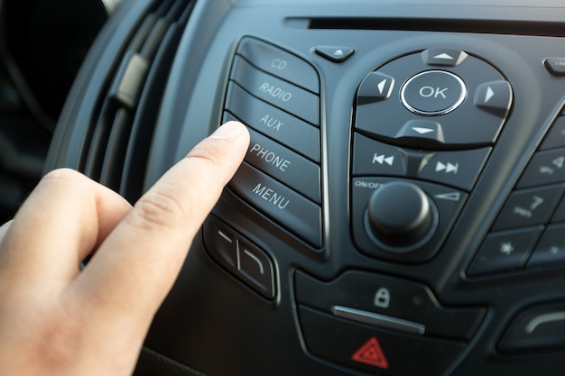 Close de dedo feminino pressionando o botão de rádio no painel de controle do carro