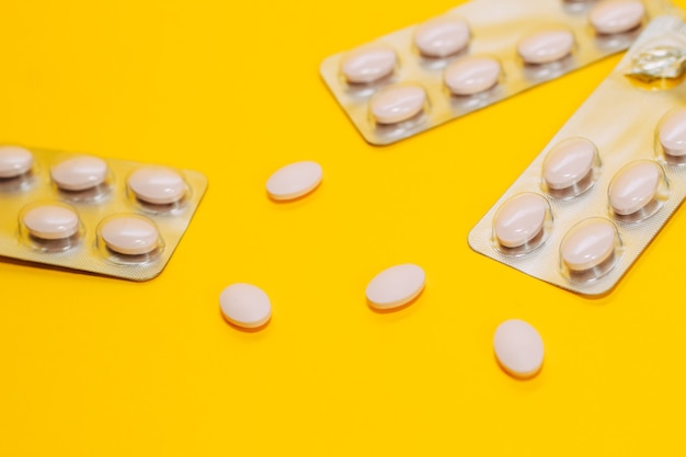 Close de diferentes comprimidos e vitaminas estão espalhados em um fundo amarelo, comprimidos em uma embalagem