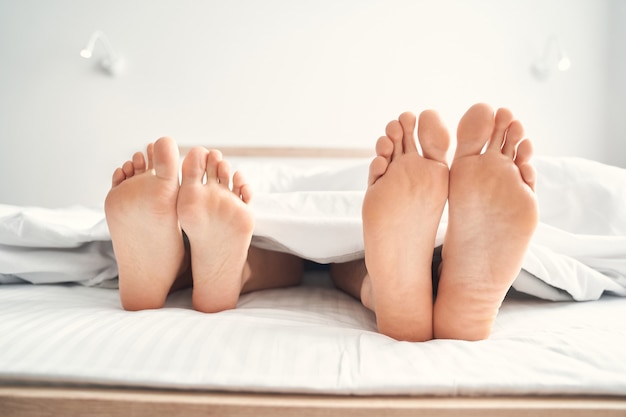 Close de dois pares de pés descalços de um casal caucasiano deitado sob o cobertor
