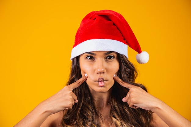 Foto close de jovem com chapéu de papai noel, fazendo caretas.