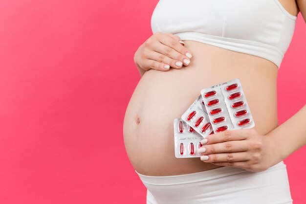 Close de mulher grávida segurando suplementos maternos