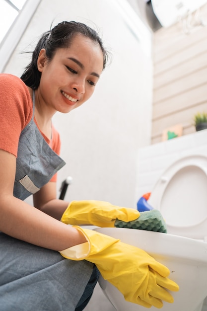 Close de mulheres asiáticas usando luvas limpando o banheiro com uma esponja no banheiro