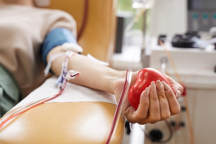 Close de paciente com tubos em seu braço apertando a bola em sua mão enquanto doa o sangue