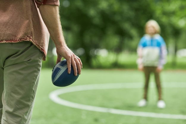 Foto close de pai e filho jogando futebol americano juntos ao ar livre no parque com foco na mão segurando o espaço de cópia da bola