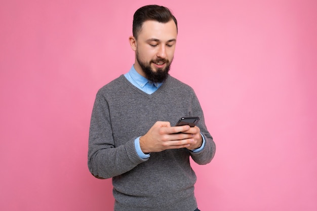 Close de perfil lateral Foto de um jovem bonito, positivo e bonito, vestindo uma roupa casual elegante, poising isolado no fundo com um espaço vazio segurando na mão e usando o messagi do telefone celular