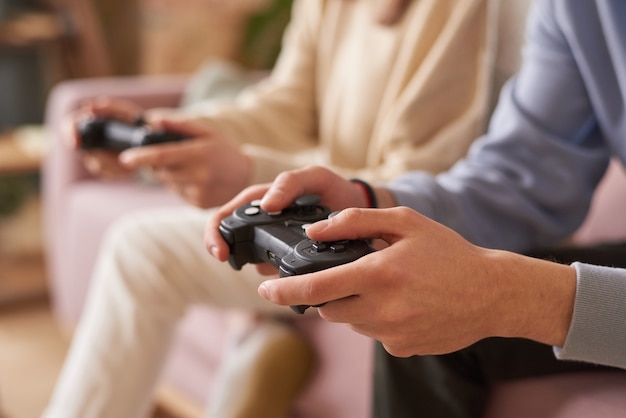 Close de pessoas sentadas no sofá com joysticks e jogando videogame em equipe