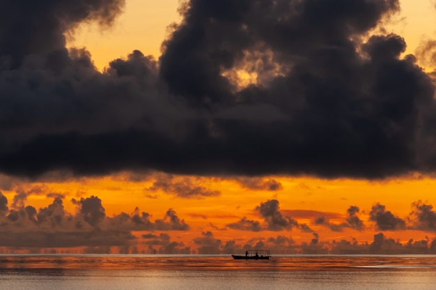 Close de um barco de pesca em um horizonte laranja com uma grande nuvem escura sobre ele