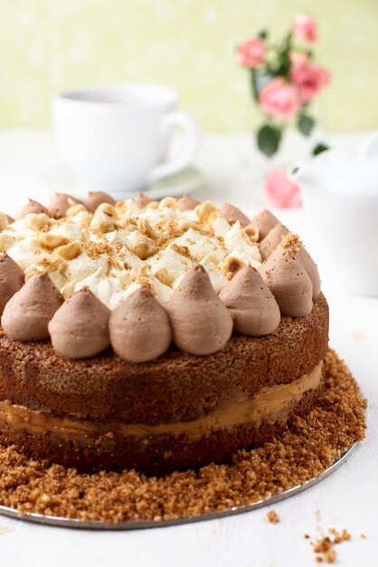 Close de um bolo de chocolate com cobertura de caramelo e nozes em uma superfície de madeira clara.