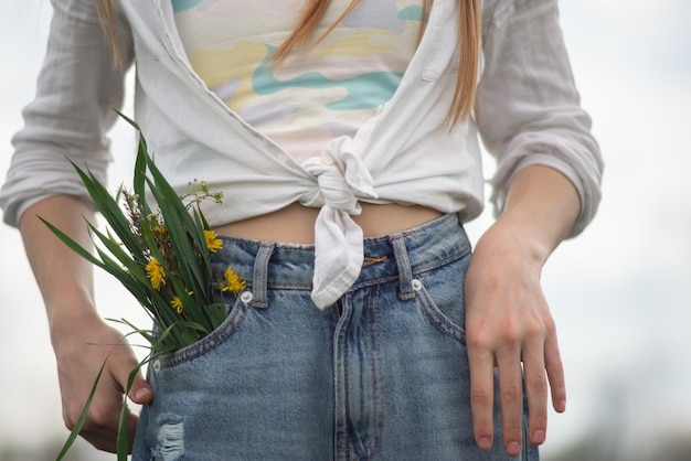 Close de um buquê de flores silvestres do bolso da calça jeans de uma adolescente