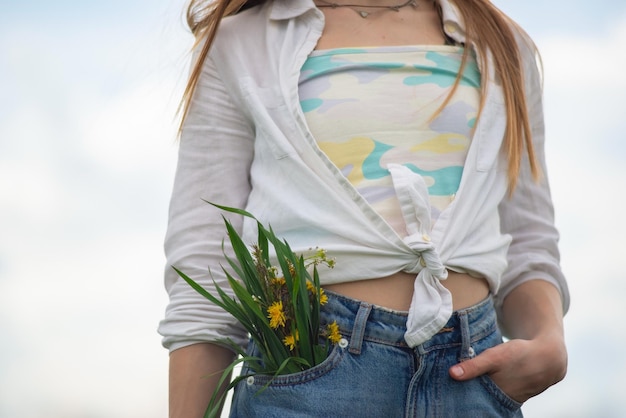 Close de um buquê de flores silvestres do bolso da calça jeans de uma adolescente