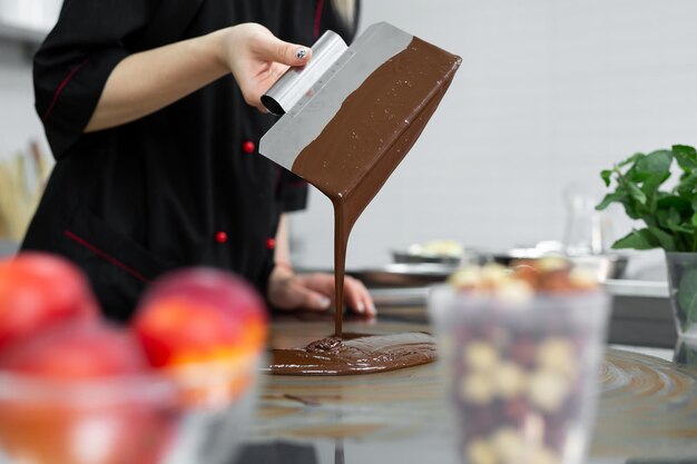 Close de um chef confeiteiro usando espátulas temperando chocolate derretido