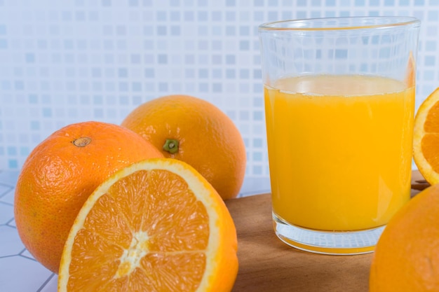 Close de um copo de suco de laranja espremido em uma mesa com laranjas ao redor