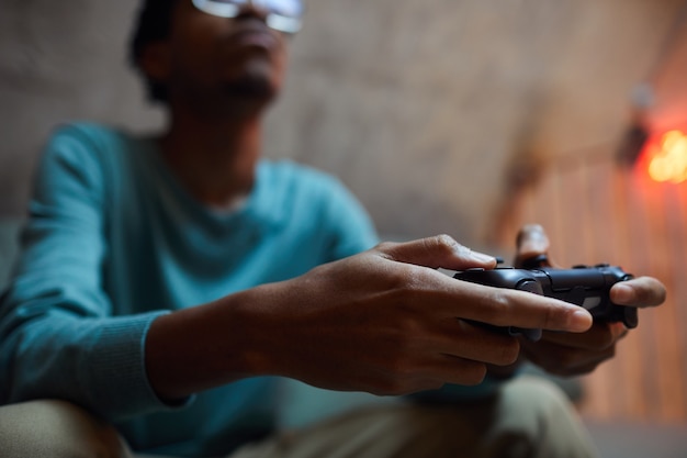 Foto close de um homem afro-americano contemporâneo segurando o controle do gamepad enquanto joga videogame