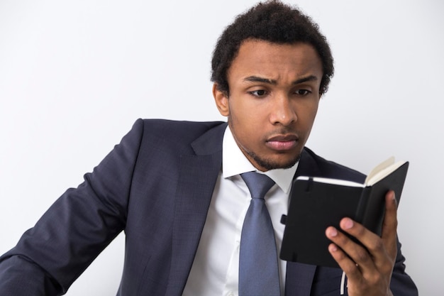 Close de um homem afro-americano lendo um pequeno caderno preto e parecendo sério. Conceito de se preparar para uma reunião do conselho.