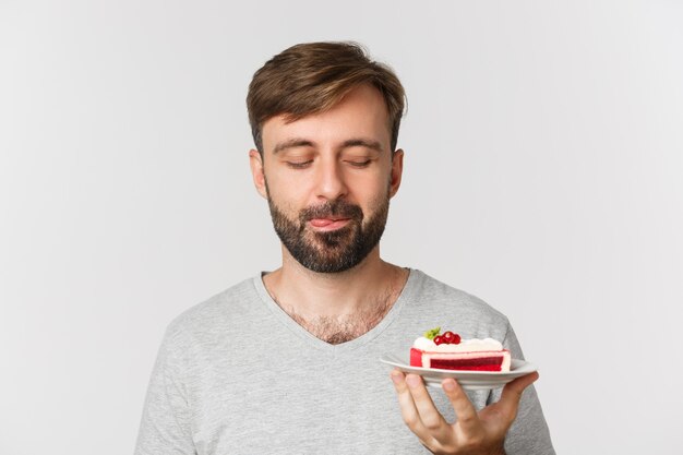 Close de um homem barbudo bonito, sorrindo e olhando para um bolo saboroso