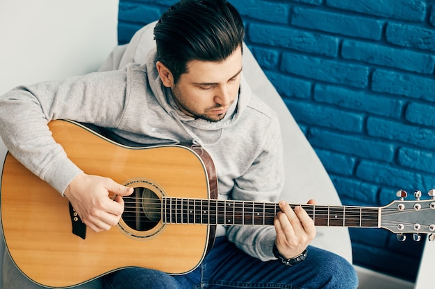 Close de um homem bonito tocando guitarra com uma parede azul