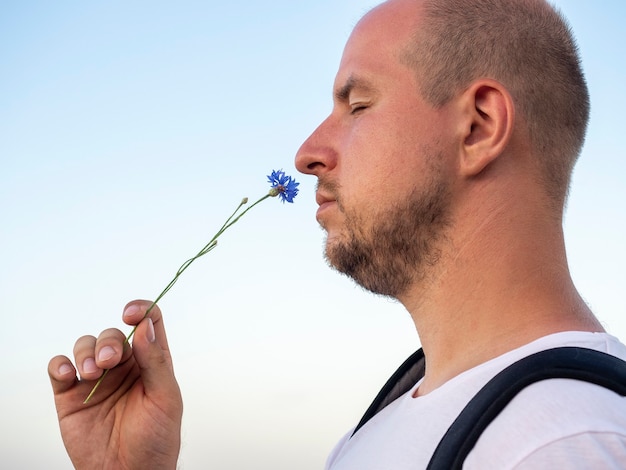 Close de um homem careca com os olhos fechados, cheirando uma flor.