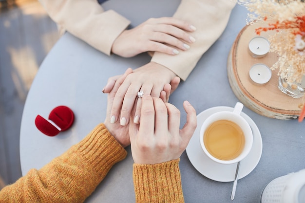 Close de um homem colocando uma aliança no dedo da namorada na mesa durante o encontro em um café